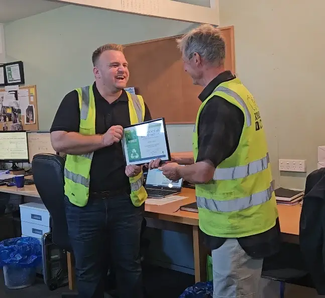 Celebrating years of excellence with mark lesliewebp | Rubbish Direct Two Men in High visibility Vests Exchange a Framed Certificate in an Office Setting Smiling at Each Other