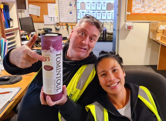 Neville yearsjpg | Rubbish Direct Two Coworkers in Highvisibility Vests Pose for the Camera While Holding a Large Bottle of Tomintoul 15 year old Whisky in a Cluttered Officeworkshop